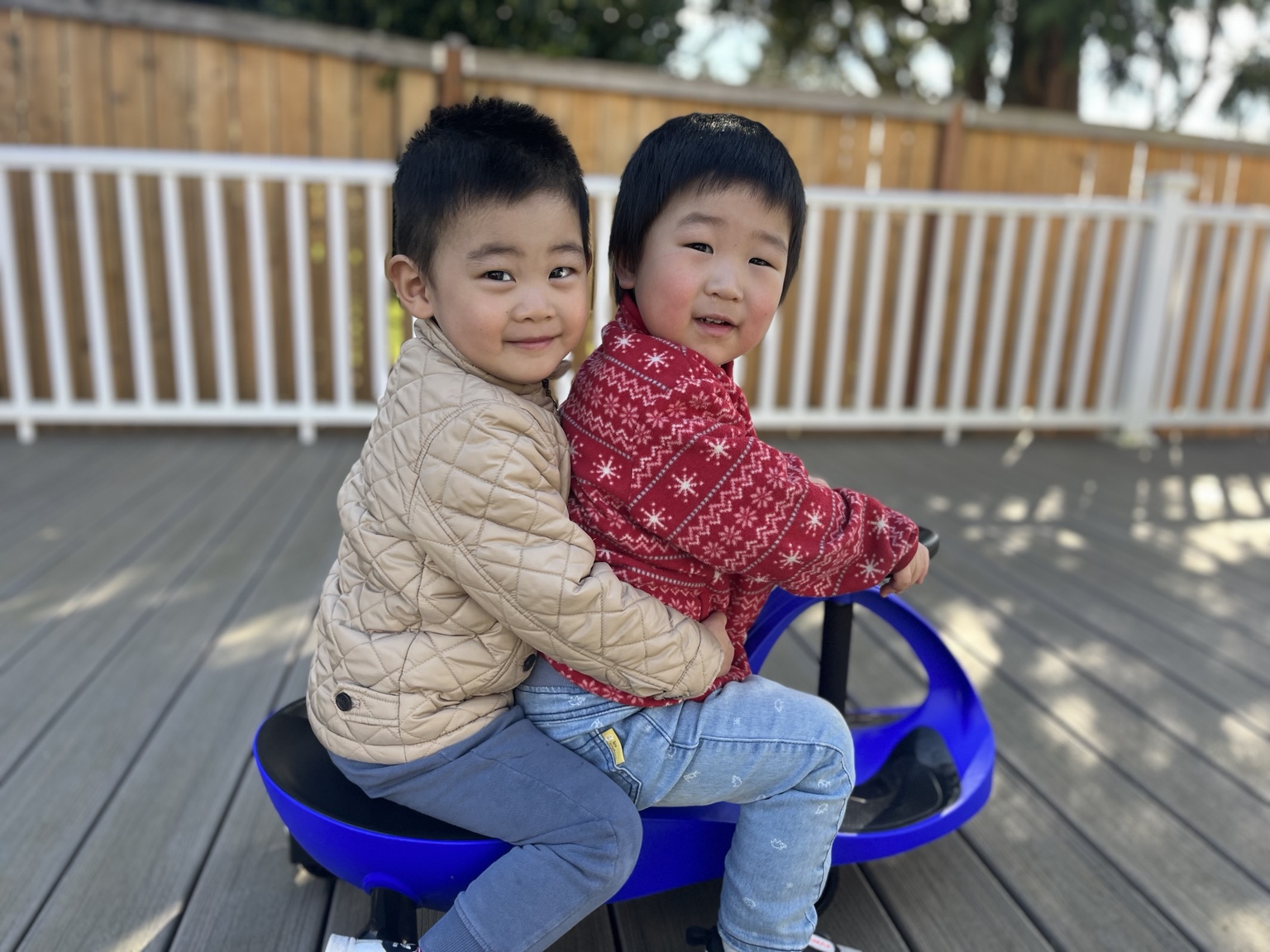 Two children smiling while riding together on an outdoor toy
